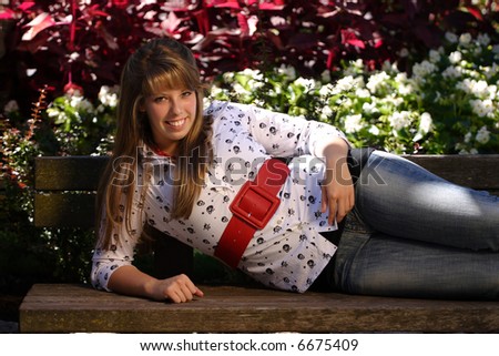 A tight shot of a pretty yong teenage girl lying down on a park bench.