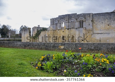 Defence walls and buildings of old medieval village of Saint Emilion with blooming flowers and lawn in Gironde, France.