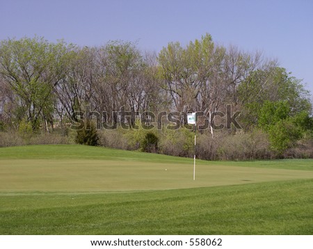 A golf ball lies a few feet from the hole on a beautiful green golf course early on a clear spring day