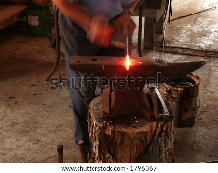 Sparks fly as blacksmith hammers incandescent steel right out of the forge. (Motion blur on man and hammer)