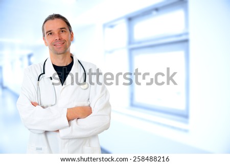 friendly young doctor with crossed arms in front of hospital background