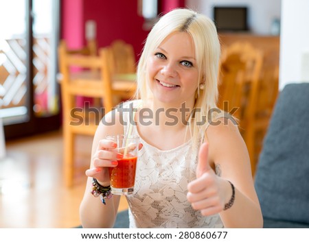 young blond woman is drinking red juice and smiling in to the camera