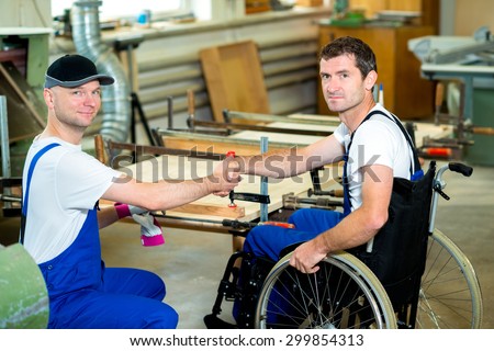 disabled worker in wheelchair in a carpenter's workshop with his colleague