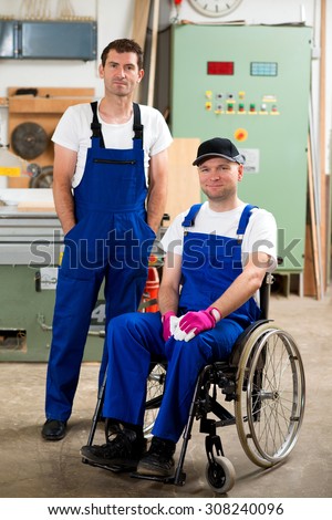 disabled worker in wheelchair in a carpenter\'s workshop with his colleague
