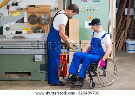 disabled worker in wheelchair in a carpenter\'s workshop with his colleague