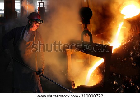 Hard work in the foundry, worker controlling iron smelting in furnaces, too hot and smoky working environment