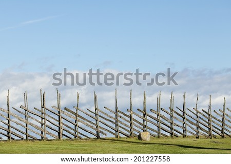 An old wood fence with a green country field behind it. Estonia, Saaremaa