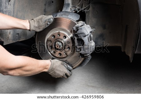 Car mechanic hands replace brakes in garage. Mechanic technician worker installing car wheel at maintenance.  Worker changing brake disc. Brake disc installation concept.