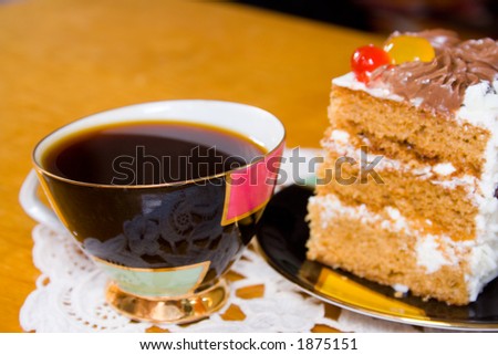 Cup of coffee and slice of creamy cake with fruits and chocolate (focused on front of a cup)