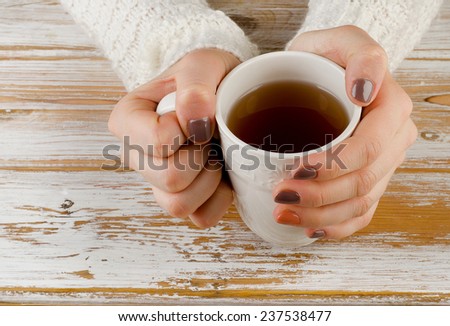 Woman holding hot cup of tea over    wooden background .