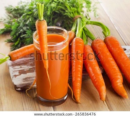 Fresh carrot juice and organic raw carrots on a wooden table.