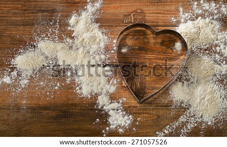 Flour and Heart-shaped cookie cutter on a worn wooden  desk.