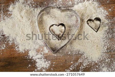 Flour and Heart-shaped cookie cutters on  worn wooden  desk.