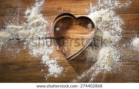White flour and Heart-shaped cookie cutter on a worn wooden  desk.