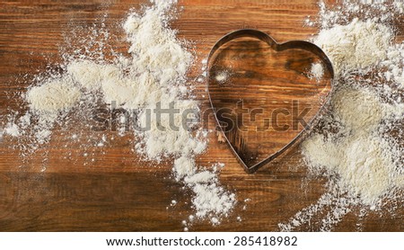 Flour and Heart-shaped cookie cutter on a worn wooden  desk.