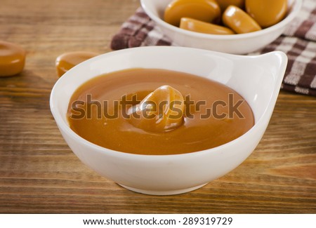 Caramel candies and sauce on  a old  wooden background. Selective focus