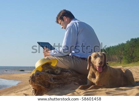 The man sits on seacoast with a dog and the computer
