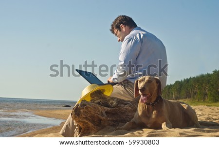 The man sits on beach with a dog and the computer