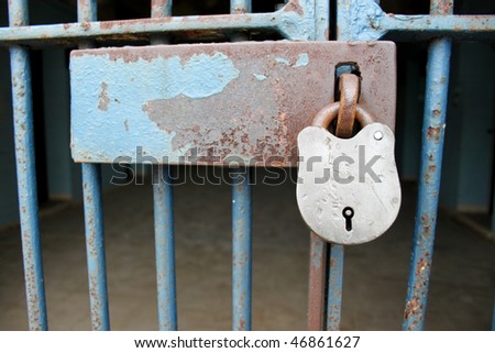 Padlock on the cell door of a prison.  Focus on the padlock with copy space room on the latch.  Dark and gloomy bars and cell in background.  The rust suggests a long stay.