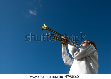 Young boy playing trumpet in white shirt against deep blue sky