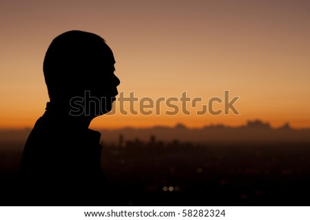 Silhouette profile of a man at sunrise with urban city behind.  Male Asian, Japanese.