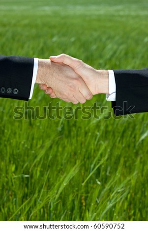 Two businessman shake hands against a green field ground with loads of copy space.