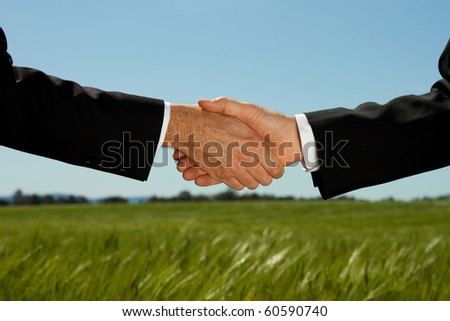 Two businessman shake hands with a land and property field background with plenty of copy space.