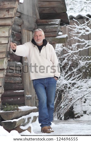An attractive middle-aged man stands near a log home