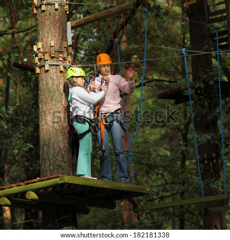 mother and daughter in climbing equipment to overcome obstacles between high trees