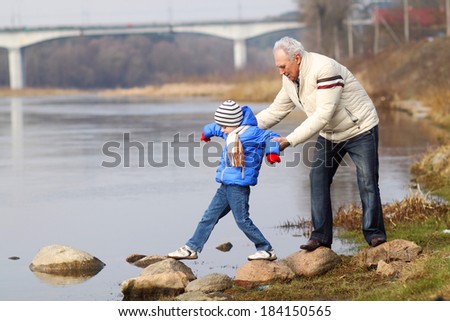 Grandfather and grandson are crossing the river on the stones. Grandfather and grandchild