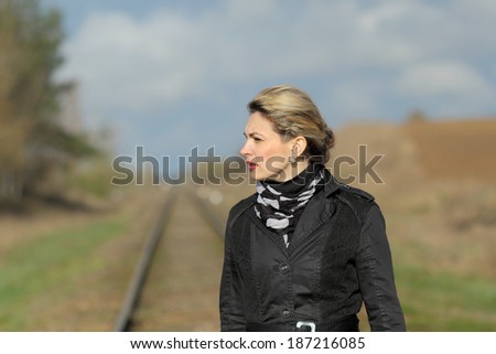 Woman in a black coat and gloves with an old suitcase walking along railway sleepers