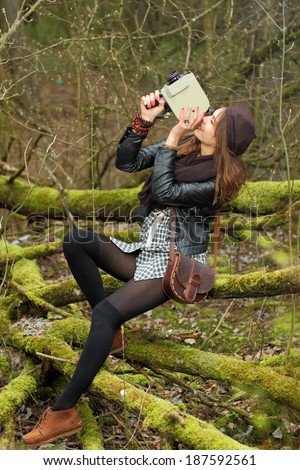 Hipster girl is shooting a film in the woods on a vintage movie camera