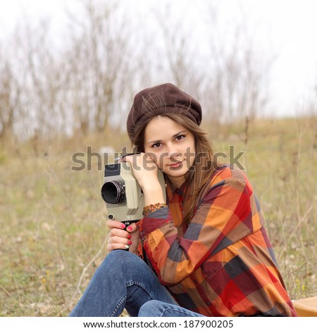 Hipster girl in a plaid shirt makes movies on a vintage movie camera.