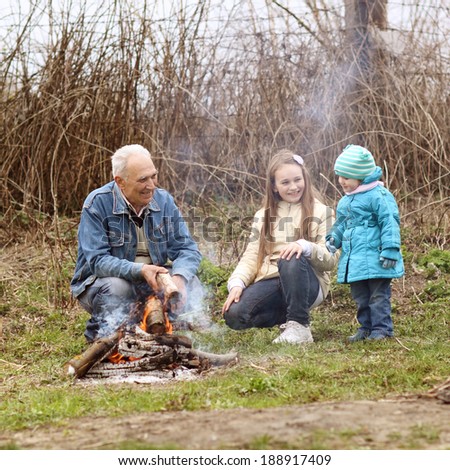 Grandfather with two grandchildren sitting around the campfire. Grandfather and grandchild