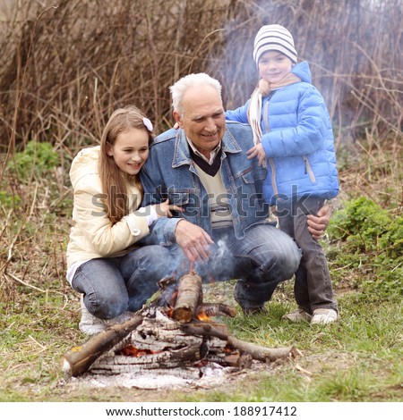 Grandfather with two grandchildren sitting around the campfire. Grandfather and grandchild