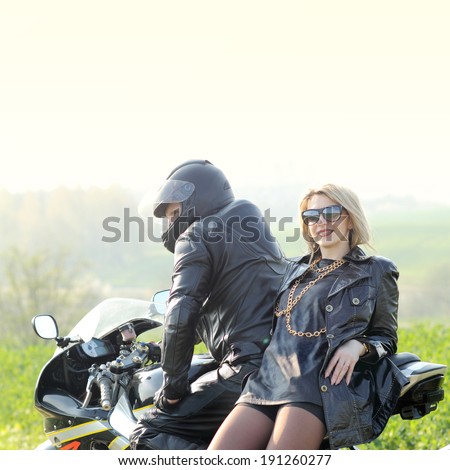 Beautiful blonde with a biker posing near a sports bike. Beautiful couple with a motorcycle at sunset