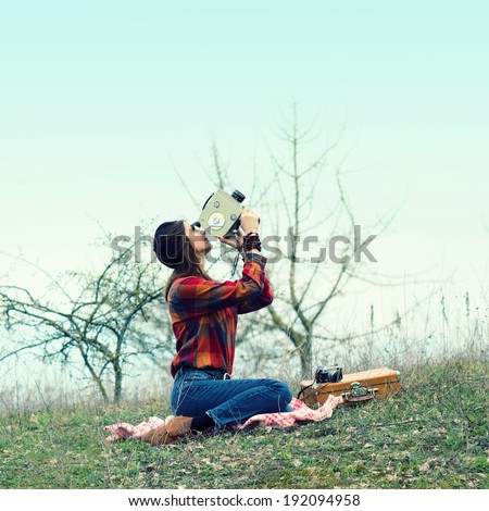 Beautiful hipster girl in a beret makes movies on vintage movie camera. pictures of the sky sitting on rug