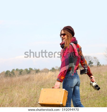 Beautiful hipster girl in a beret with vintage suitcase and vintage movie camera. modern girl travels to wildlife with vintage camera. view from the back