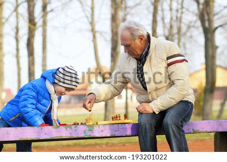 Grandfather and grandson playing chess on a bench outdoors