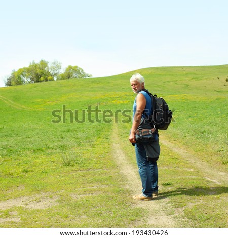 An elderly man with a backpack walking along the road. Elderly man enjoys traveling and photography nature.