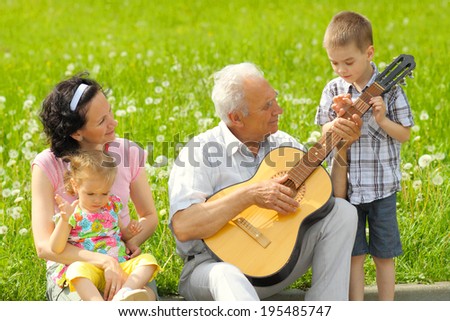 Grandfather playing guitar to his daughter and grandchildren outdoors. romantic portrait of three generations with the guitar.