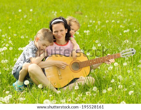 young mother plays the guitar for his young children on nature. happy mother and children playing a guitar outdoors