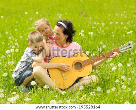 young mother plays the guitar for his young children on nature. happy mother and children playing a guitar outdoors