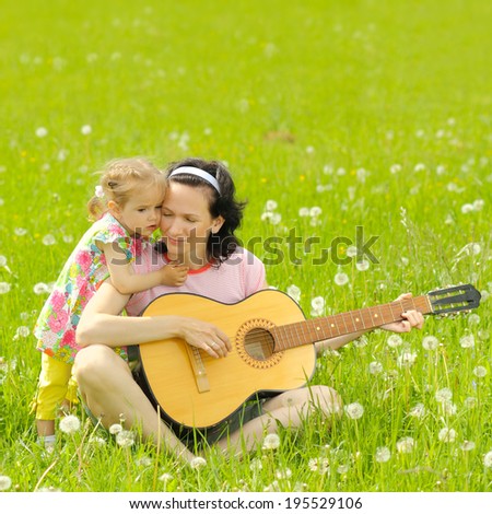 young mother plays the guitar for her little daughter on green meadow
