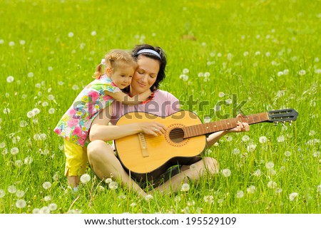 young mother plays the guitar for her little daughter on green meadow