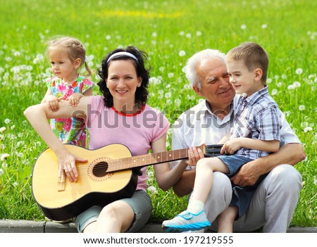 young happy mother playing guitar for her young children and grandfather. romantic portrait of three generations with the guitar.