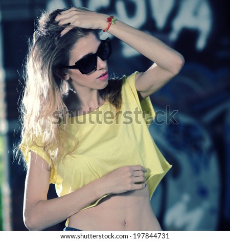 Beautiful funky girl in sunglasses against graffiti wall in background having fun with skateboard. Urban lifestyle shot.