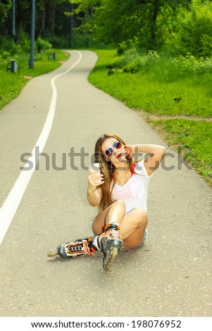 sexy girl on roller skates sitting on the road and photographed herself. Outdoor lifestyle. Nice girl doing Selfie.