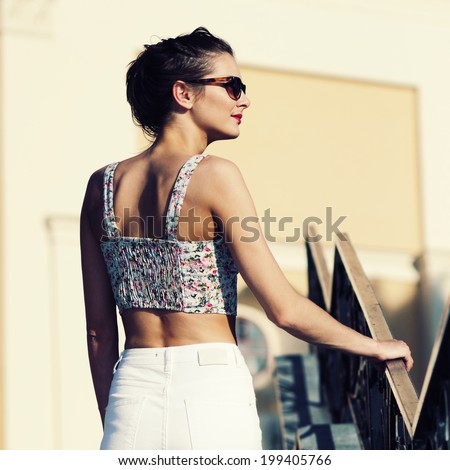 Portrait of a young beautiful girl in sunglasses and white trousers walking on the streets of old european city. View from the back. Outdoors