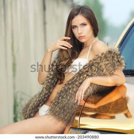 Beautiful sexy girl in bikini and in fur cape posing on a background of golden car. sexy lady near the golden car
